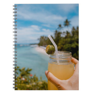 Person holding mason jar with filled with juice at notebook