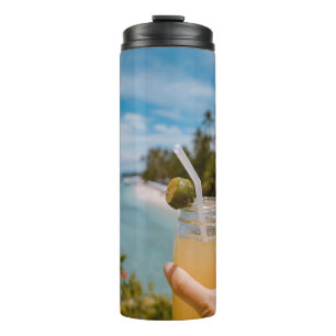 Person holding mason jar with filled with juice at thermal tumbler