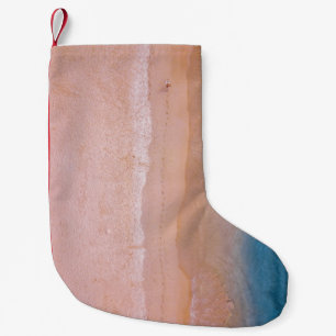 Person walking on sand near seashore leaving foot small christmas stocking