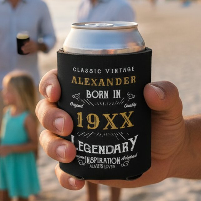 Personalised Birthday Add Your Name Year Legendary Can Cooler (Black and gold can cooler in a hand with a beach background.)