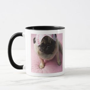 Pug dog with eye mask on head sitting on bed, mug