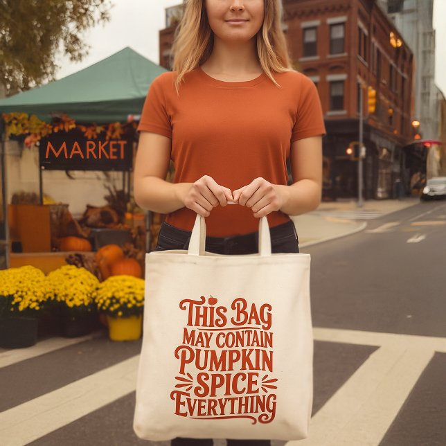 Pumpkin Spice Everything Funny Fall Warning Label Tote Bag (woman holding a funny pumpkin spice grocery tote bag in front of an urban market stall)