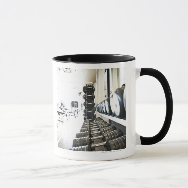 Row of free weights in foreground and exercise mug (Right)