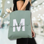 Sage Green Modern Script Name Monogram Tote Bag<br><div class="desc">Personalised Elegant Sage Green Trendy Modern Script Name Monogram Tote Bag. Add a touch of sophistication to your everyday style with this chic tote bag. Featuring a sleek white initial centred on a soft sage green background, overlaid with a flowing black script name, this clean and modern design appears on...</div>