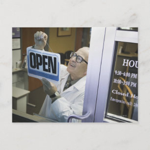 Senior male pharmacist hanging 'Open' sign in Postcard
