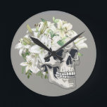 Silent Bloom: Skull & White Lilies Round Clock<br><div class="desc">Embrace the poetic beauty of life and death with Silent Bloom: Skull & White Lilies. This striking design combines the raw symbolism of a human skull with the purity and grace of white lilies, creating a powerful contrast between mortality and innocence. Perfect for those who love gothic art, botanical themes,...</div>