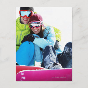 Snowboarder couple sitting on snow postcard