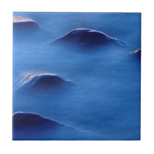 Sunset on rocks protruding through foamy water tile