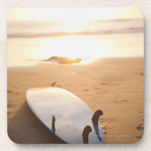 Surfboard laying on beach at sunset coaster