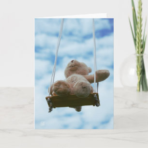 Teddy bear on a swing with a cloudy blue sky. holiday card