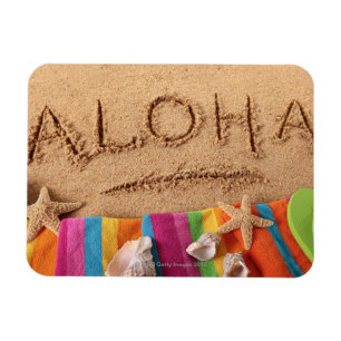 The word Aloha written on a sandy beach, with Magnet