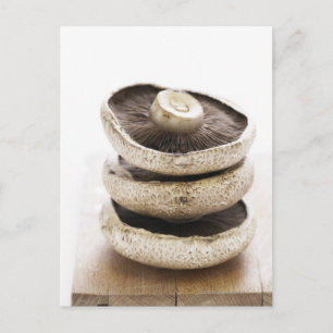 Three flat mushrooms in pile on wooden board, postcard