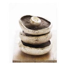 Three flat mushrooms in pile on wooden board,