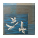 Three White Seagulls Flying Over the Water Ceramic Tile<br><div class="desc">Need to get away? Do it by choosing this painting by artist Tara Friel representing three seagulls flying over the water. The sight of the waves of the ocean and the vivid colours make this design very realistic.</div>