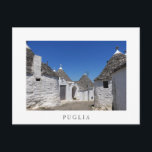 Trulli houses in Puglia white postcard<br><div class="desc">Postcard with traditional white plaster trulli houses with stone tiles in conical roofs in a small street in the town Alberobello,  Itria Valley in Puglia,  Italy with a white border and the text: 'Puglia'.</div>