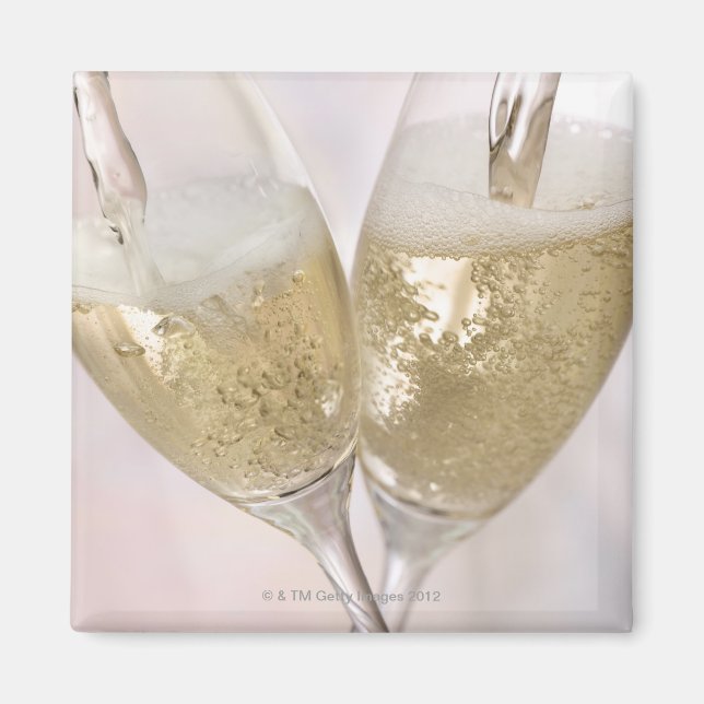 Two champagne flutes being filled with sparkling magnet (Front)