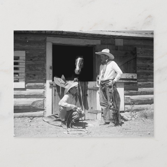 Two cowboys standing next to a barn with a horse postcard (Front)