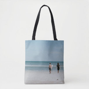 Two person walking on coast tote bag