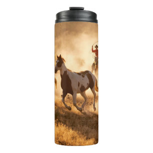 Two western cowboys riding horses, roping wild hor thermal tumbler