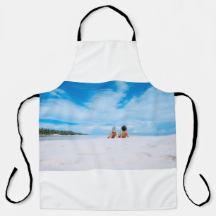 Two women lying on white sand facing beach under b apron