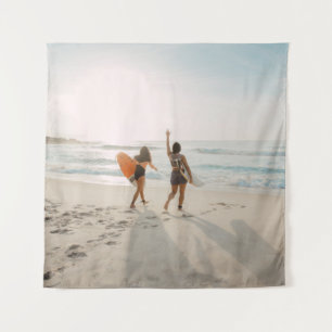 Two women walking towards the ocean carrying surfb tapestry