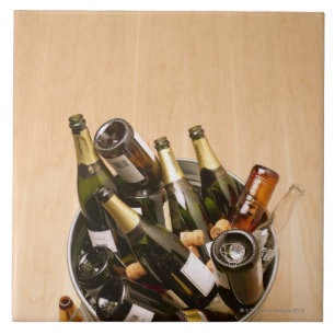 Waste bin full of empty champagne bottles on ceramic tile