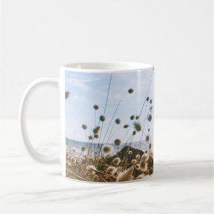 WHITE FLOWERS FIELD NEAR BODY OF WATER UNDER BLUE COFFEE MUG