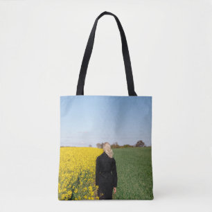 Woman in black coat standing on green grass field tote bag