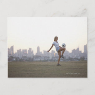 Woman kneeing soccer ball in urban park postcard