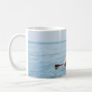 Woman on an inflatable float in the ocean pointing coffee mug