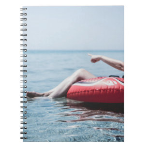 Woman on an inflatable float in the ocean pointing notebook