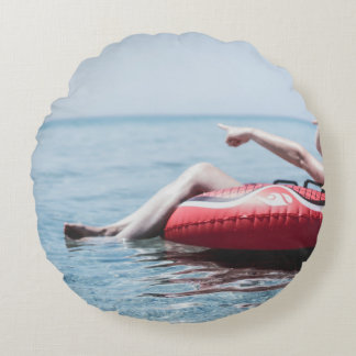 Woman on an inflatable float in the ocean pointing round cushion