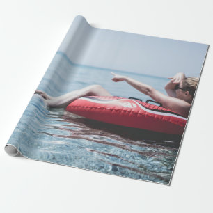 Woman on an inflatable float in the ocean pointing wrapping paper