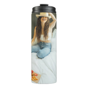 Woman sitting on bed holding her hat thermal tumbler