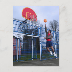 Young man playing basketball outdoors postcard