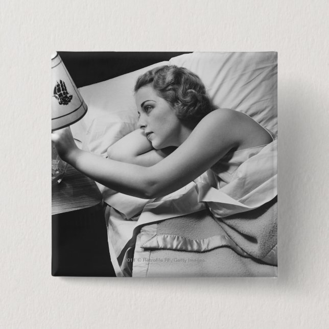 Young woman lying on bed turning off lamp on 15 cm square badge (Front)