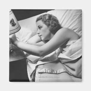 Young woman lying on bed turning off lamp on magnet