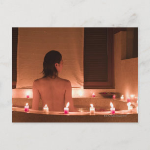 Young woman taking bath with flower petals postcard